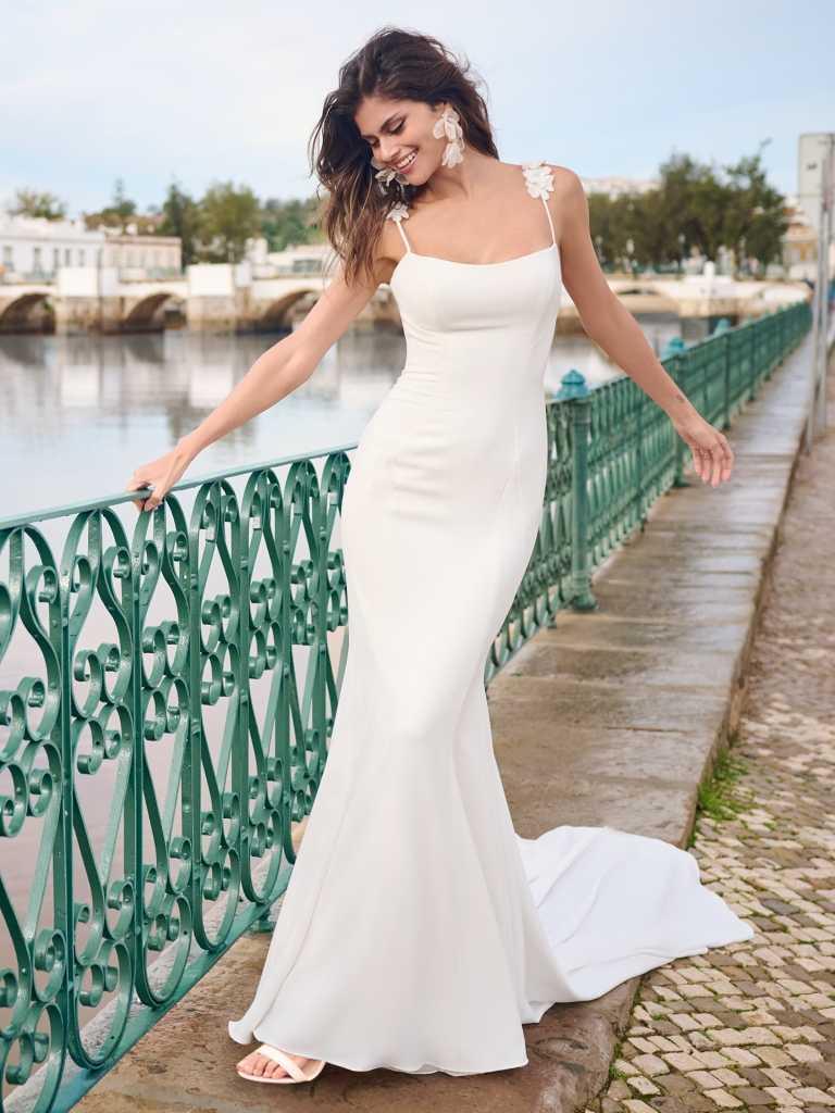 A woman in white dress standing next to a green fence.