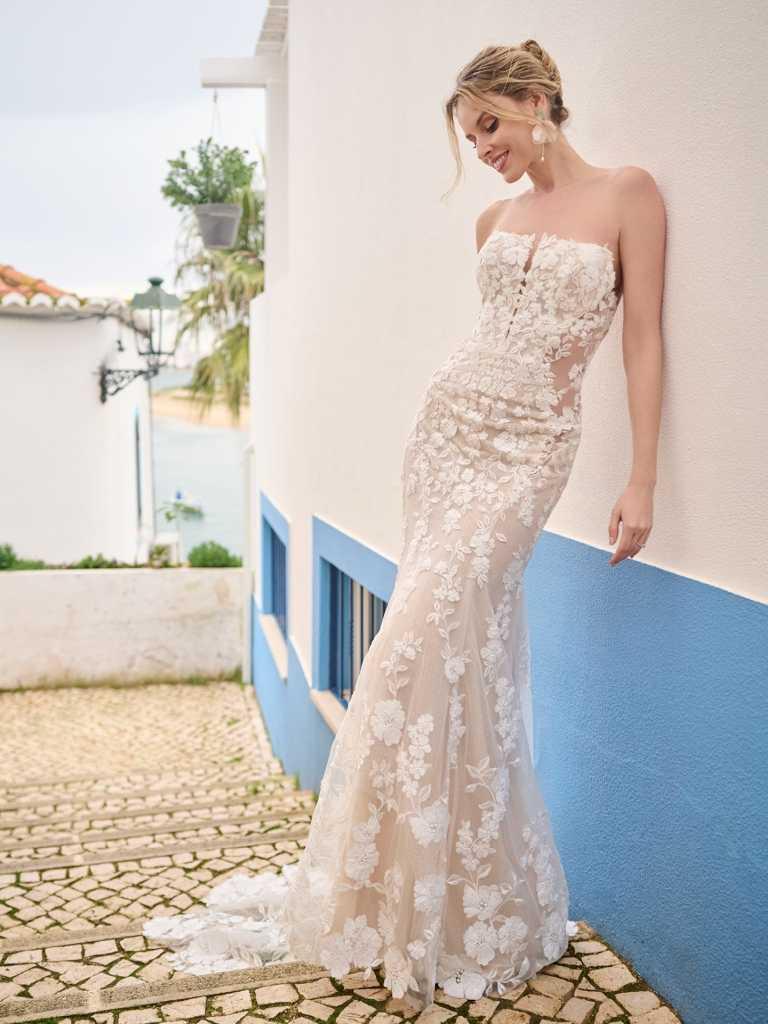 A woman in a white dress leaning against a wall.