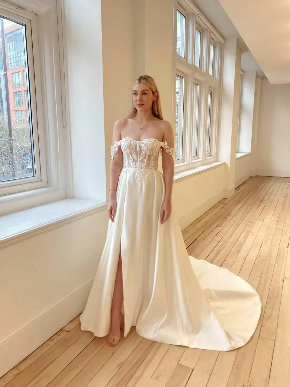 A woman in a white dress standing next to a window.