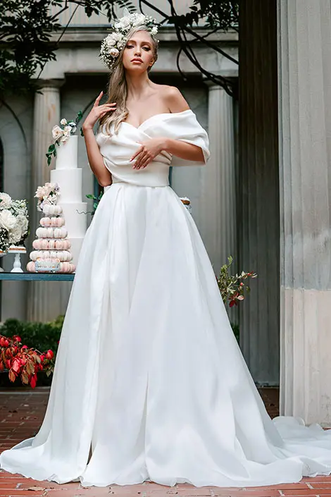 A woman in white dress standing next to cake.