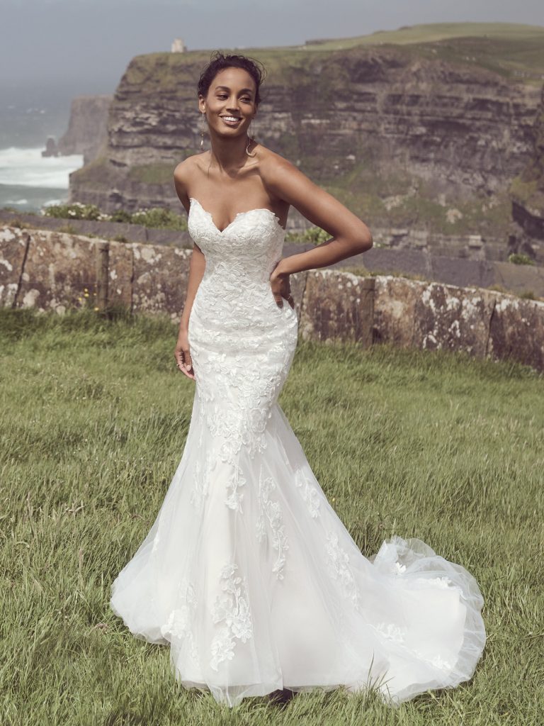 A woman in a white dress standing on top of a grass covered hill.