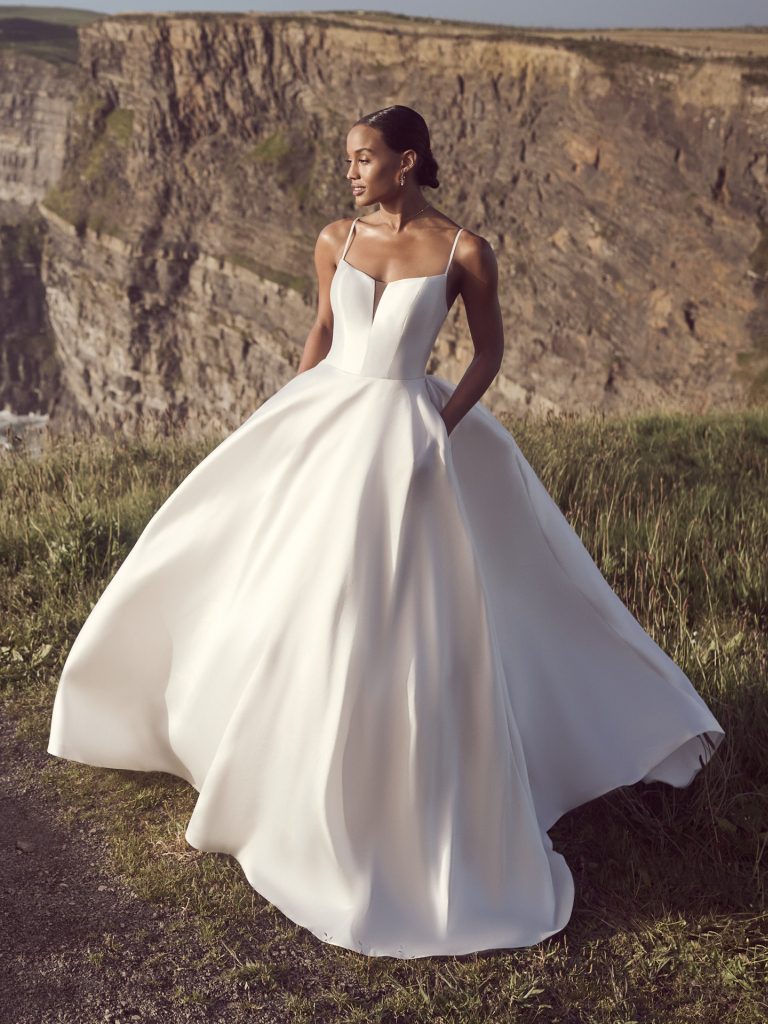 A woman in a white dress standing on top of a grass covered hill.